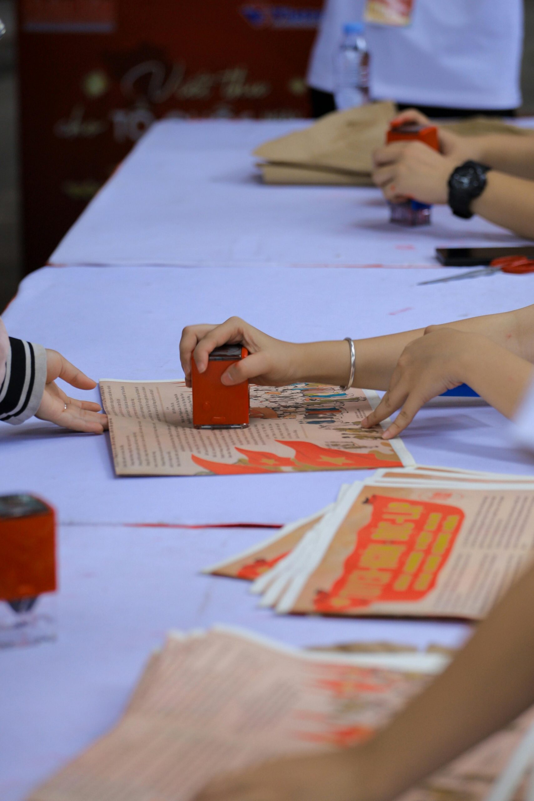 People hand-stamping red prints on paper sheets during a cultural event in Hanoi, Vietnam.